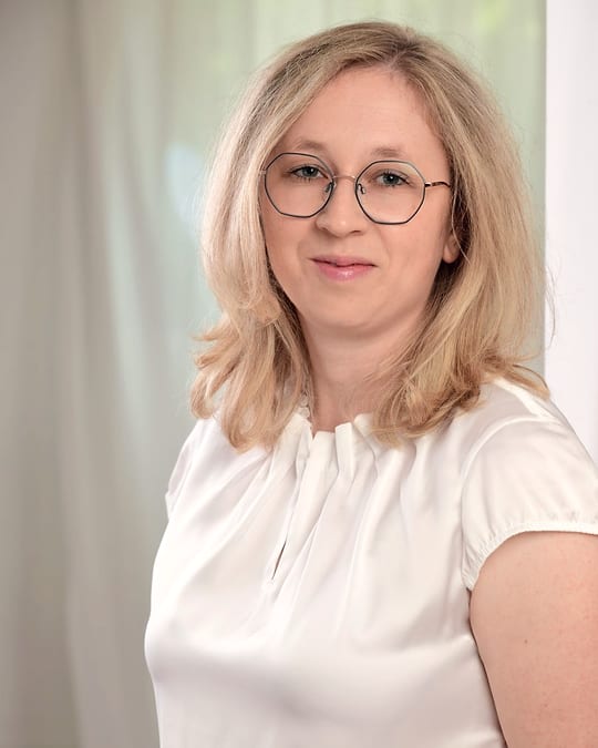 Miriam Althaler, blond mit Brille und heller Bluse, lächelt ruhig und offen in die Kamera.