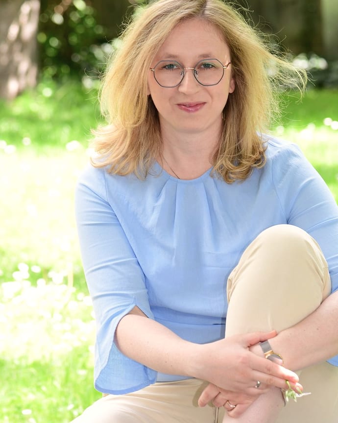 Miriam Althaler sitzt entspannt auf einer sonnigen Wiese, in hellblauer Bluse, und schaut freundlich in die Kamera.